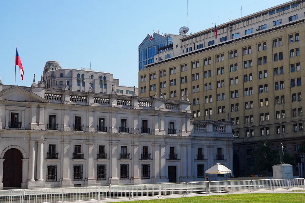 畫面左側的白色建築是智利的總統府，拉莫內達宮 (La Moneda Palace)。位於是右側較高的黃色現代建築是智利國防部的所在地。